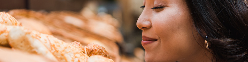 selective focus of cheerful asian woman smiling while smelling bread in supermarket