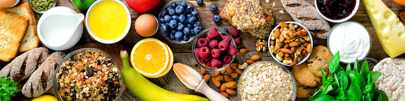 Healthy breakfast ingredients, food frame. Granola, egg, nuts, fruits, berries, toast, milk, yogurt, orange juice, cheese, banana, apple on wooden rustic background, top view, copy space